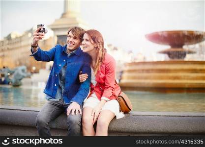 Couple taking camera selfie at Trafalgar Square fountain, London, UK