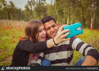 Couple taking selfie picture with their mobile phone in field of red poppies.