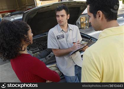 Couple talking to mechanic by open car hood