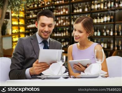 couple, technology and leisure concept - smiling young woman looking into boyfriends or husbands menu on tablet pc computer over restaurant or wine bar background. couple with menus on tablet pc at restaurant