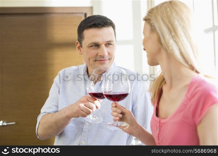 Couple toasting red wine glasses in kitchen