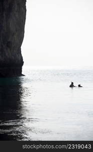 Couple tourists snorkeling in the sea in front of ancient cliff in sunny day. White sky backgrounds. Summer season. Koh Hong Island, Andaman sea, Krabi, Thailand. High key. Silhouette. Bright sunlight. Copy space.