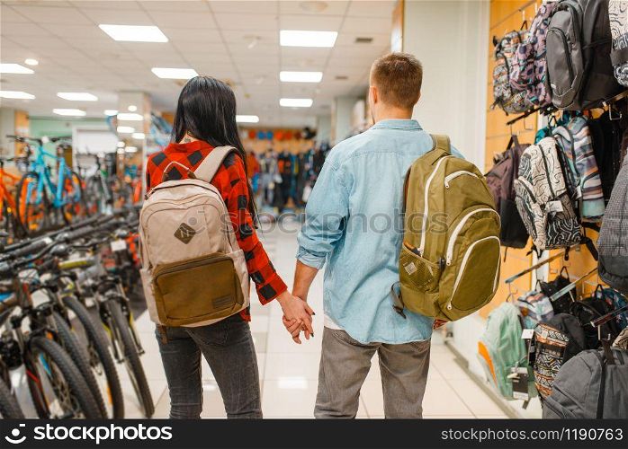 Couple trying on backpacks for travelling, shopping in sports shop. Summer season extreme lifestyle, active leisure store, customers buying tourist equipment