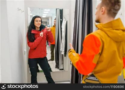 Couple trying on jackets for ski or snowboarding, sports shop. Winter season extreme lifestyle, active leisure store, customers with protect equipment. Couple trying on jackets for ski or snowboarding