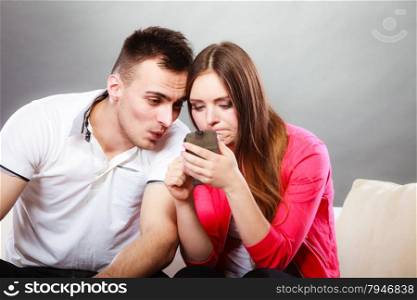 Couple use mobile phone texting and sending messages. Surprised woman and man using new technology surfing internet sitting on couch at home.