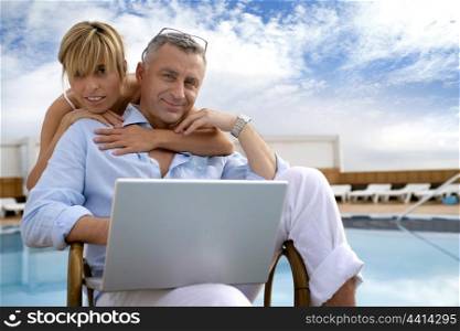 Couple using a laptop by the poolside