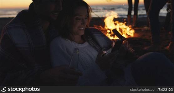 Couple using cell phone during beach party with friends drinking beer and having fun