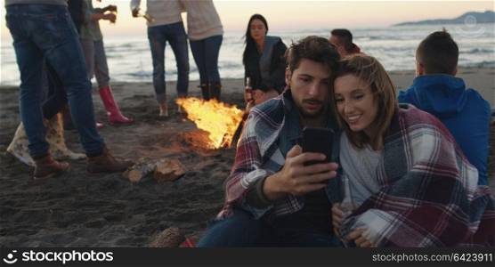 Couple using cell phone during beach party with friends drinking beer and having fun