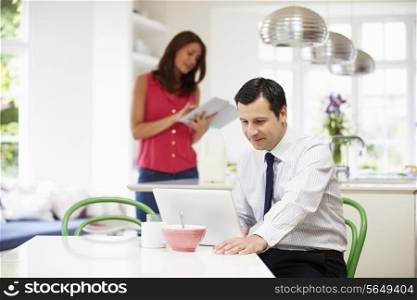 Couple Using Digital Devices At Breakfast Table