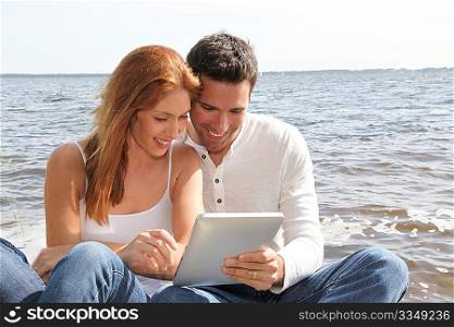 Couple using electronic tablet by a lake