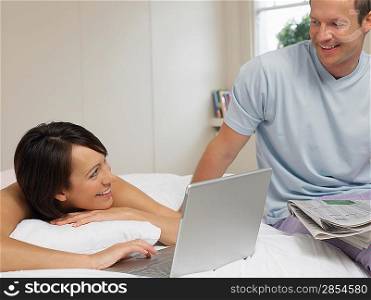 Couple Using Laptop and Newspaper