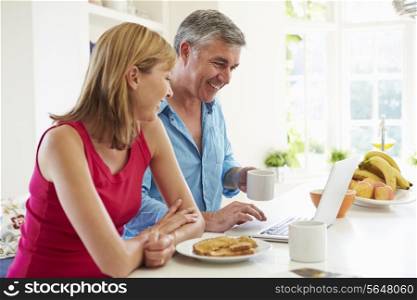 Couple Using Laptop Whilst Having Breakfast In Kitchen