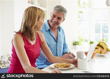 Couple Using Laptop Whilst Having Breakfast In Kitchen