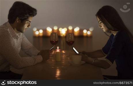 Couple using mobile phone while having dinner in restaurant at night