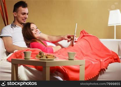 Couple using tablet browsing web internet.. Couple using tablet browsing web online. Woman and man using new technology surfing internet relaxing laying on couch at home.