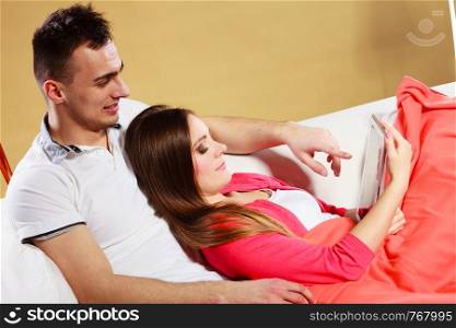 Couple using tablet browsing web online. Woman and man using new technology surfing internet relaxing laying on couch at home.. Couple using tablet browsing web internet.