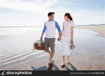 Couple Walking Along Beach With Picnic Basket