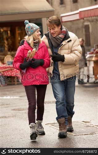Couple Walking Along Snowy Town Street In Ski Resort