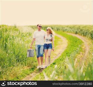 Couple walking in field, man holding in his hand vintage suitcase, tinted photo