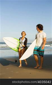 Couple walking on beach, carrying surfboards