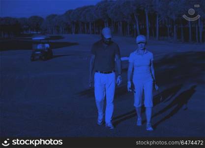 couple walking on golf course. young couple walking to next hole on golf course. man carrying golf bag duo tone