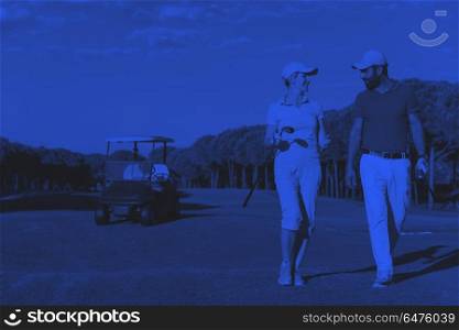 couple walking on golf course. young couple walking to next hole on golf course. man carrying golf bag duo tone