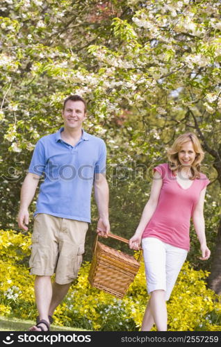 Couple walking outdoors with picnic basket smiling