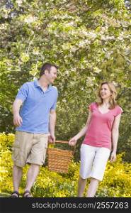 Couple walking outdoors with picnic basket smiling
