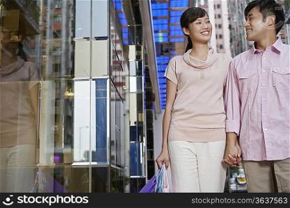Couple walking past store, looking in eyes and smiling