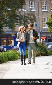 Couple Walking Through Park With Takeaway Coffee