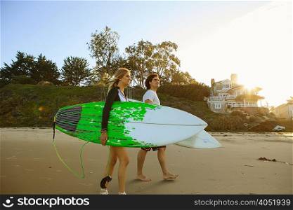 Couple walking towards sea, carrying surfboards