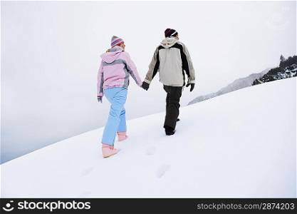 Couple walking up snow-covered hill back view low angle view