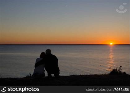 Couple watching a romantic sunset by the coast