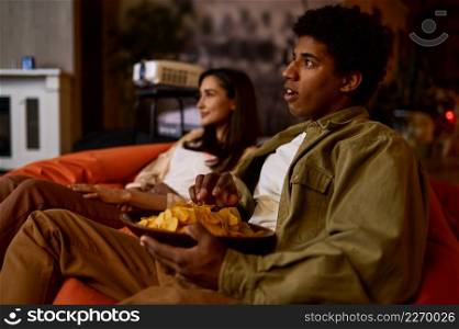 Couple watching movie on domestic cinema projector at home. Young man and woman enjoy time together. Emotional young couple watching movie at home