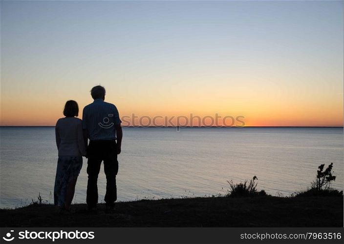 Couple watching sunset hand in hand by the coast