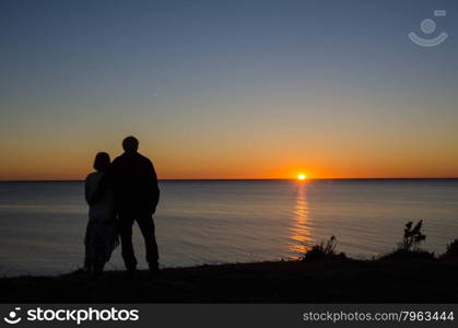 Couple watching the sunset at the horizon by the sea