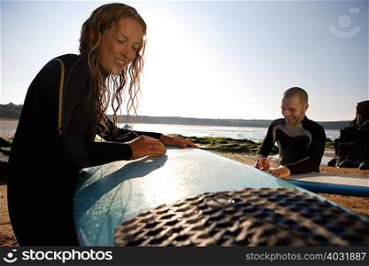 Couple waxing their surfboards smiling