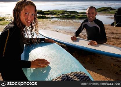 Couple waxing their surfboards smiling