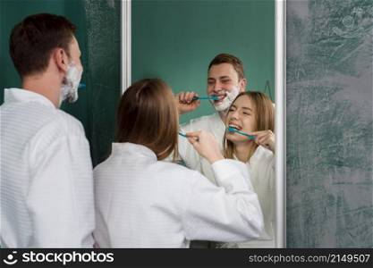 couple wearing bathrobes brushing teeth mirror