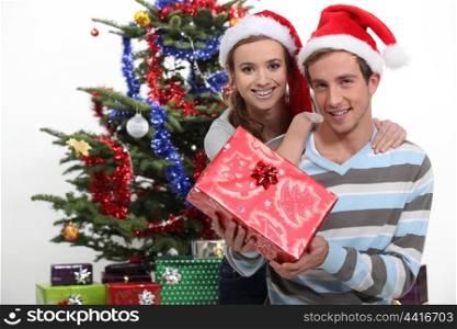 Couple wearing festive hats stood by Christmas tree