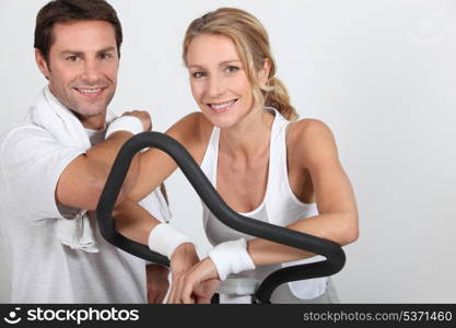 Couple wearing sportswear stood by exercise bike