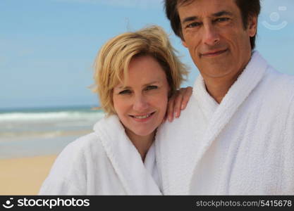 Couple wearing white bathrobes stood by the sea