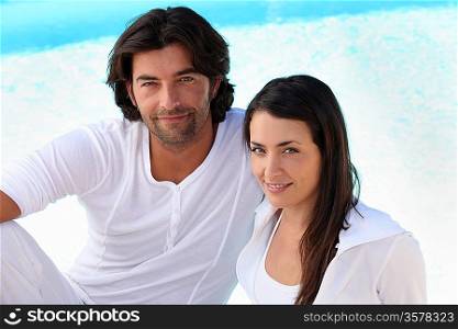 Couple wearing white clothing sat by swimming pool