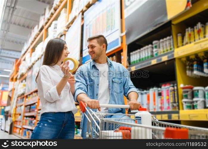 Couple with a cart buying building materials in hardware store. Customers look at the goods in diy shop. Couple with a cart buying building materials