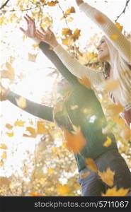 Couple with arms raised enjoying falling autumn leaves in park
