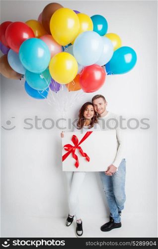 Couple with balloons and gift. Young smiling couple with balloons and big gift box