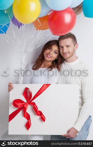 Couple with balloons and gift. Young smiling couple with balloons and big gift box