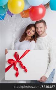 Couple with balloons and gift. Young smiling couple with balloons and big gift box