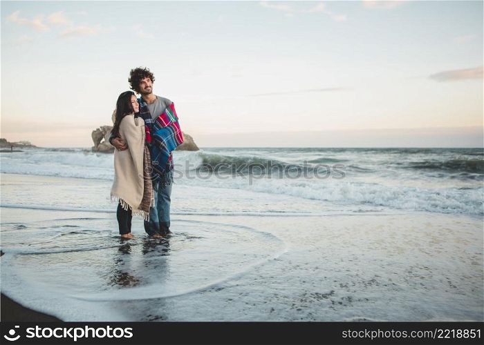 couple with blankets top feet beach water