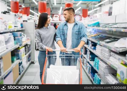 Couple with cart in a supermarket, family shopping. Customers in shop, buyers choosing consumer goods